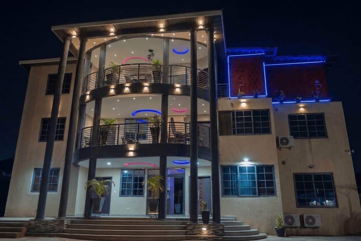The DeHideout building at night, its curved balconies lit and the rooftop pergola outlined in blue